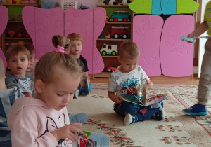 Dzieci z grupy Słoneczka siedzą na dywanie i oglądają książeczki.