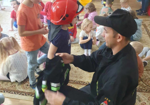 Dzieci ustawione w kolejce aby przymierzyć strój strażaka.