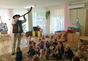 Góral Szczepan demonstruje dzieciom gre na instrumiencie jakim jest róg.
