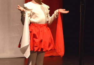 Amelka w biało-czerwonym stroju i wianku śpiewa na scenie konkursową piosenkę.