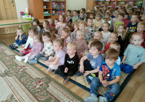 Przedszkolaki siedzą na dywanie i krzesłach z zainteresowaniem oglądają przedstawienie.