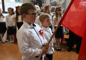 Piotruś K. i Natan trzymają flagę Polski. Wszyscy zebrani goście śpiewają hymn.