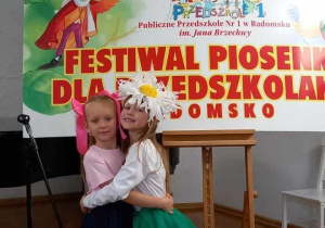 Julcia i Oliwka szczęśliwe, przytulaja się do siebie na tle kolorowej reklamy festiwalu.
