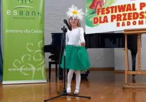 Oliwka w zielonej spódniczce, białej bluzce i pięknej opasce z kwiatem na głowie prezentuje na scenie swoją piosenkę.