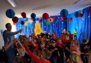 Przedszkolaki zebrane w sali balowej, słuchają instrukcji do tańca , wydawanych przez Pana Wodzireja.