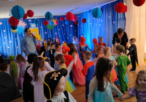 Przedszkolaki zebrane w sali balowej, słuchają instrukcji do tańca , wydawanych przez Pana Wodzireja.