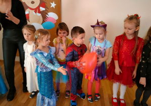 Grupka przedszkolaków w swoich bajkowych przebraniach podczas zabawy z balonikiem.