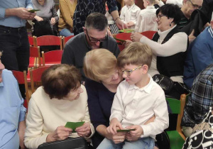 Antoś z grupy 5-latków siedzi na kolanach u swojej babci. Z boku druga babcia uśmiecha sie do niego.