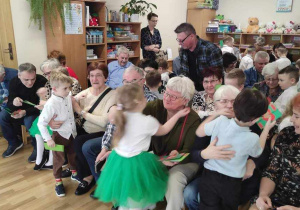 Wnuczęta wręczają swoim babciom i dziadziusiom laurki i przytulaja sie mocno do swoich bliskich.