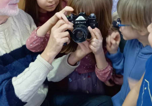 Dzieci oglądają różne rodzaje sprzętu fotograficznego zaprezentowanego przez pana fotografa.