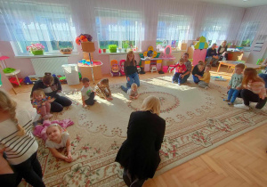 Dzieci bawią się na dywanie w kółeczku do znanej piosenki o dinozaurach.