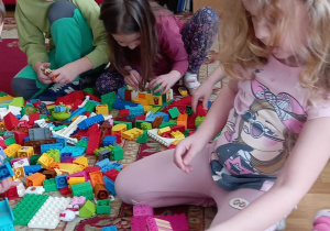 Dwie dziewczynki i chłopiec wykonują budowlę z klocków lego.
