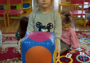 Dziewczynka trzyma niebieską kostkę z kolorowymi kołami.