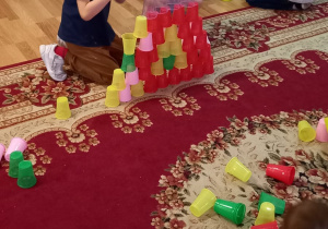 Dzieci układają na podłodze wieże z kolorowych kubeczków jednorazowych.