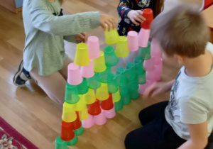 Dzieci układają na podłodze wieże z kolorowych kubeczków jednorazowych.