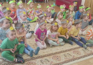 Dzieci mają na głowach opaski z emblematami słońca i motyli, siedzą na dywanie.