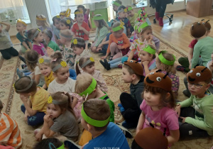 Dzieci mają na głowach opaski z emblematami słońca i motyli, siedzą na dywanie.