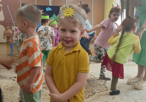 Uśmiechnięty chłopiec w żółtej koszulce, za nim tańczą inne dzieci.