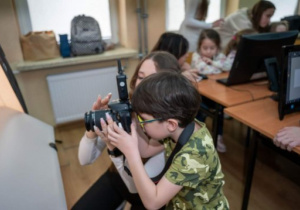 Chłopiec pod opieką dziewczyny trzymają aparat fotograficzny, chłopiec uczy się fotografować.
