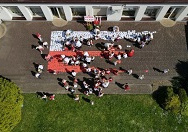 Widok z dronu. Dzieci na tarasie przedszkolnym układają biało-czerwoną flagę Polski z wyciętych serduszek w kolorach naszej flagi.