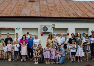 Pamiątkowe zdjęcie dzieci z grupy Żuczki z rodzicami na tarasie przedszkola. Z tyłu napis Mamo, Tato kocham Was.