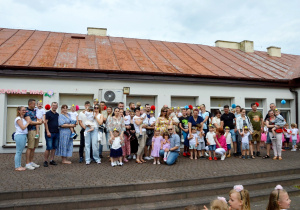 Pamiątkowe zdjęcie dzieci z grupy Słoneczka z rodzicami na tarasie przedszkola. Z tyłu napis Mamo, Tato kocham Was.