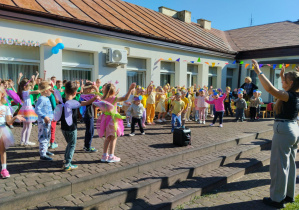 Przedszkolaki tańczą na tarasie przedszkola. Pani Kasia podaje układ taneczny.