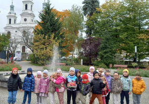 Grupa dzieci ustawionych jeden obok drugiego na tle kościoła parafialnego pw.św. Lamberta.