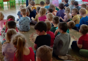 Przedszkolaki siedzą na dywanie i słuchają muzyka, który gra na trąbce.