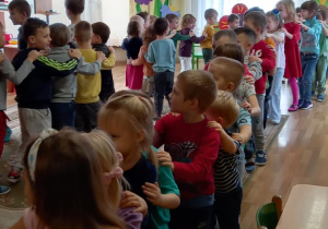 Przedszkolaki stoją jeden za drugim trzymając ręce na ramionach dziecka z przodu, utworzyły pociąg.