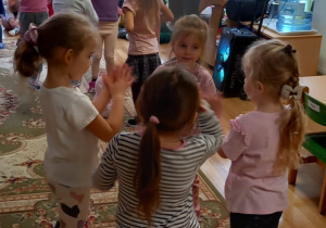 Dziewczynki stoją w dwóch czteroosobowych kołach i tańczą, muzyk gra na trąbce.