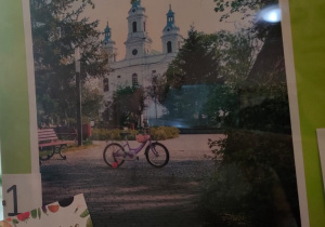 Rower dziecięcy w parku przy Placu 3 Maja w oddali widać biały kościół.