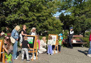 Dzieci przy sztalugach malują farbami w parku na Placu 3 Maja.
