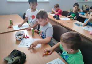 Przedszkolaki siedzą przy stolikach i kolorują bohaterów z bajki Psi patrol.
