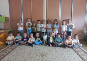 Pamiątkowe zdjęcie z psem, który siedzi pośrodku grupy przedszkolaków.