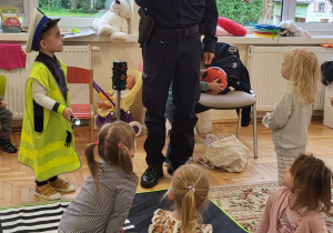 Pan policjant w mundurze demonstruje dźwięk gwizdka. Przedszkolaki są wokół niego.