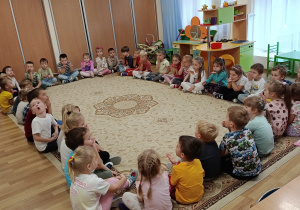 Przedszkolaki siedzą na obrzeżu dywanu i puszczają buziaki.
