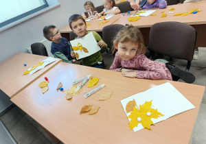 Dzieci siedzą przy stolikach i wykonują pracę plastyczną Jesienne stworki.