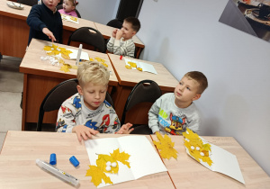 Dzieci siedzą przy stolikach i wykonują pracę plastyczną Jesienne stworki.