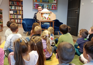 Pan bibliotekarz czyta dzieciom bajkę wykorzystując teatrzyk kamishibai - Jesienny bal w lesie.