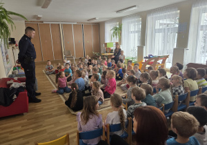 Policjant stoi przed przedszkolakami w sali przedszkolnej.