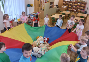 Dzieci trzymają chustę animacyjną, a na niej swoje misie.