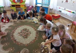 Ratownik uciska klatkę fantomu, dzieci robią to samo na misiach.