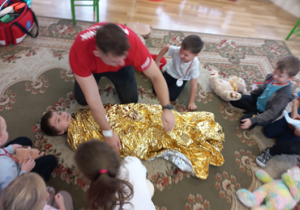 Ratownik przykrywa kocem termicznym chłopca.