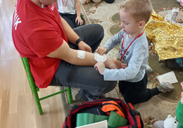 Chłopiec przykleja plaster z opatrunkiem na ręce ratownika.
