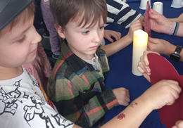 Dwóch chłopców stoi przy stole, na którym są sztuczne świece i białe kubeczki.