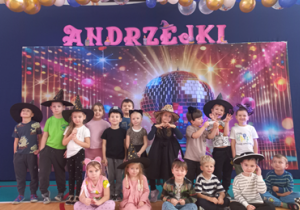 Przedszkolaki na pamiątkowym zdjęciu na tle kolorowej, dyskotekowej kuli, nad którą jest napis Andrzejki.