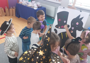 Dzieci dekorują sylwetę czarnego kota i magiczny cylinder różnymi ozdobami.