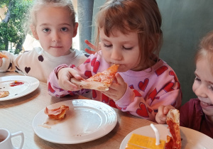 Trzy dziewczynki siedzą przy stole i jedzą pizzę.