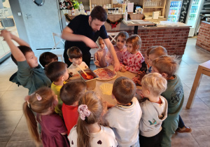 Przedszkolaki obserwują pizzermana podczas wykonywania pizzy.